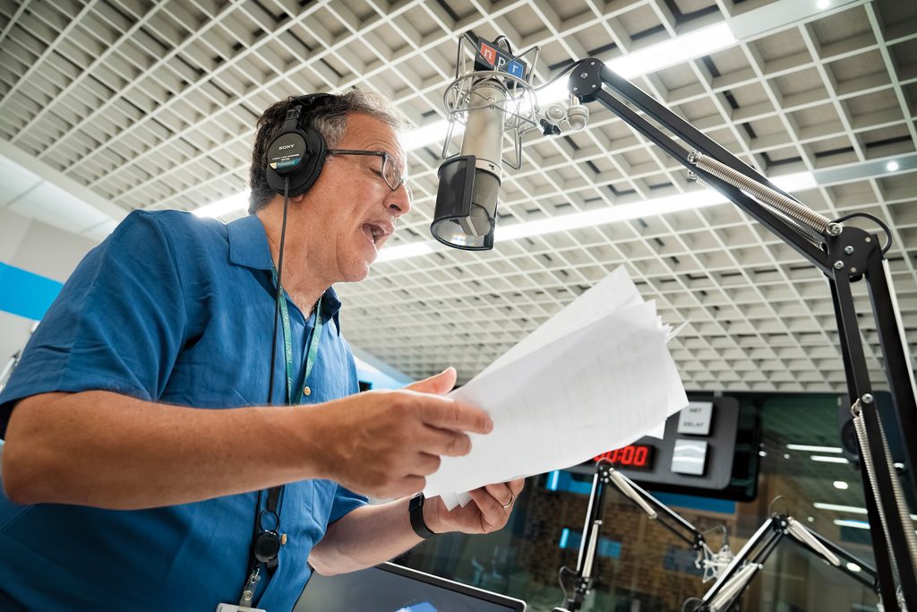 Joseph Shapiro ’75 reads the news from sheets of paper in an NPR radio station