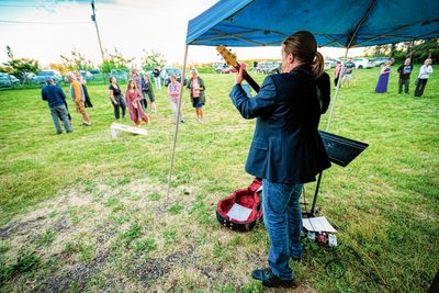 A musicial plays a guitar outdoors on a lawn under a shaded canopy