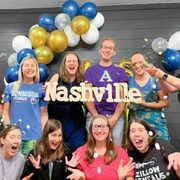 A group of friends pose for a photo with balloons and confetti, holding a sign reading: Nashville
