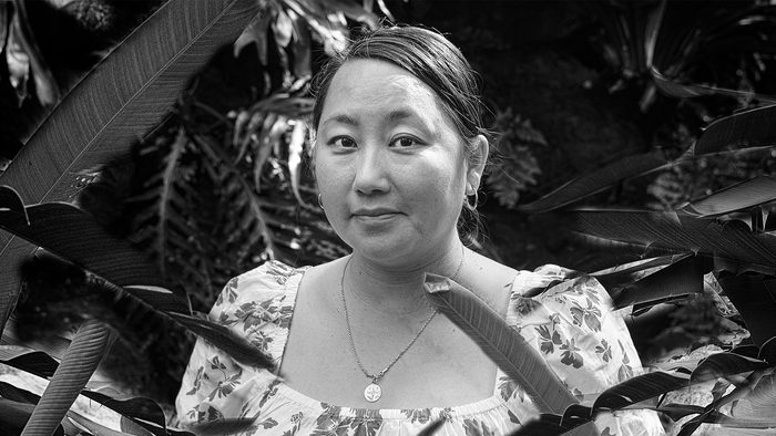 Black & white photo of Kao Kalia Yang surrounded by tropical foliage