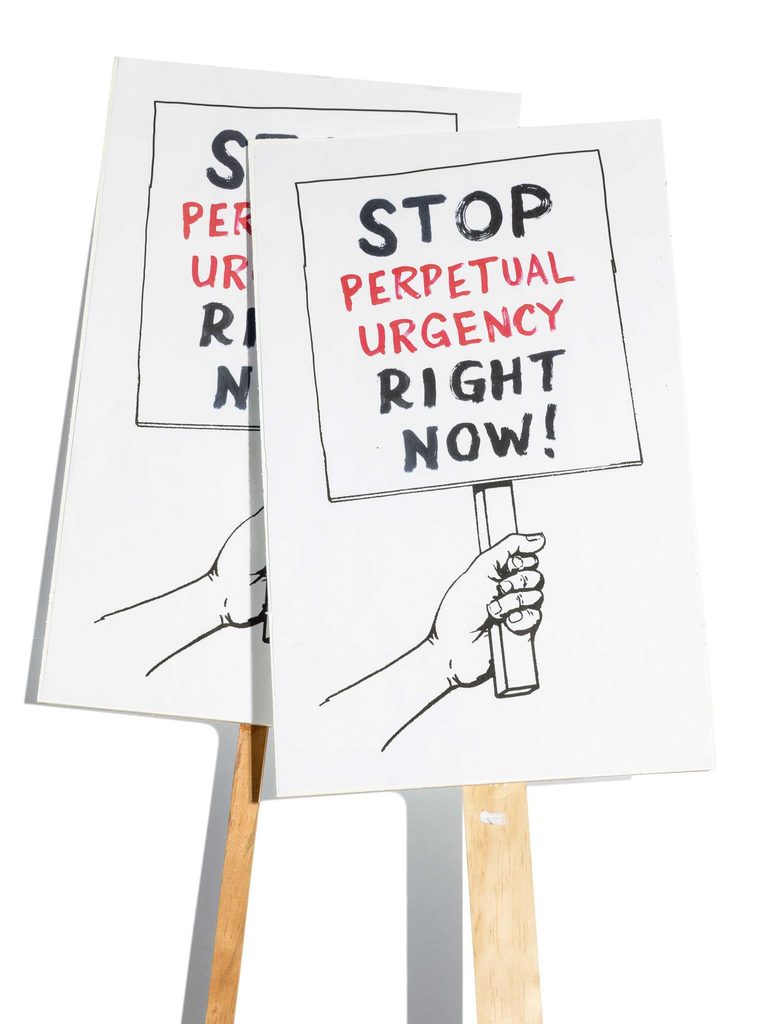posters on wooden stakes that read "stop perpetual urgency right now!"