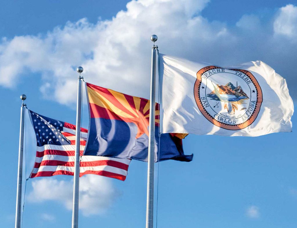 Three flags — United States, San Carlos Apache Tribe, and Arizona State flag — flying