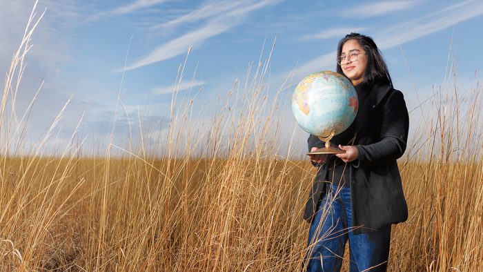 Zainab Waheed stands in the Arboretum holding a globe