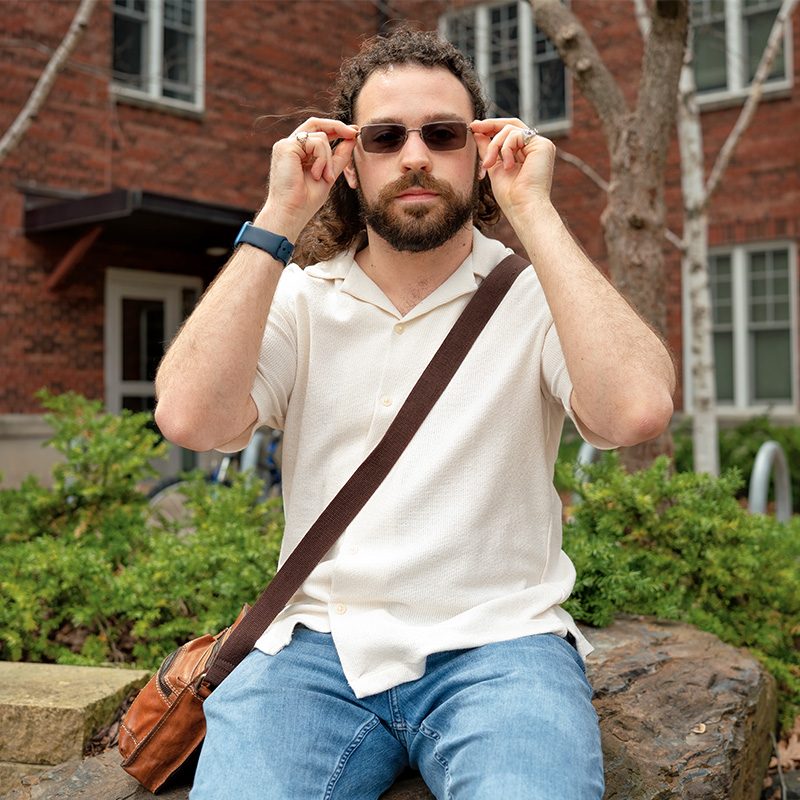 Ryan Quinn seated outdoors placing sunglasses on