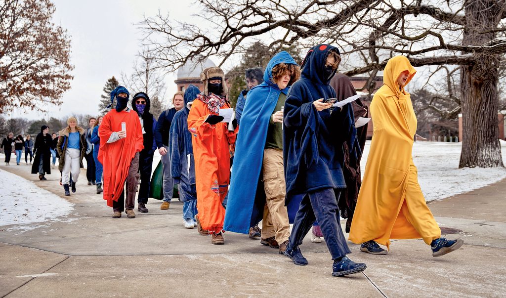 students in blankets walking in a line on the sidewalk