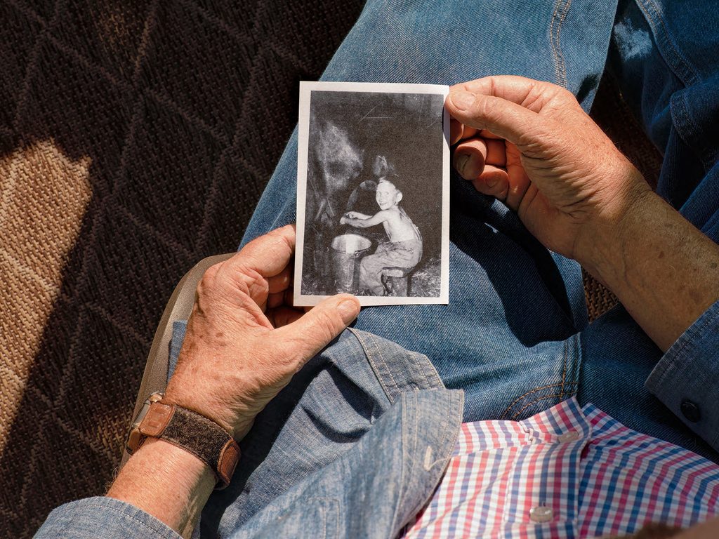 close of up Dean's hands holding a black and white photo of himself as a child milking a cow