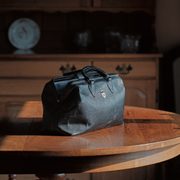 A vintage doctor's bag sits on a wooden table in a farm house