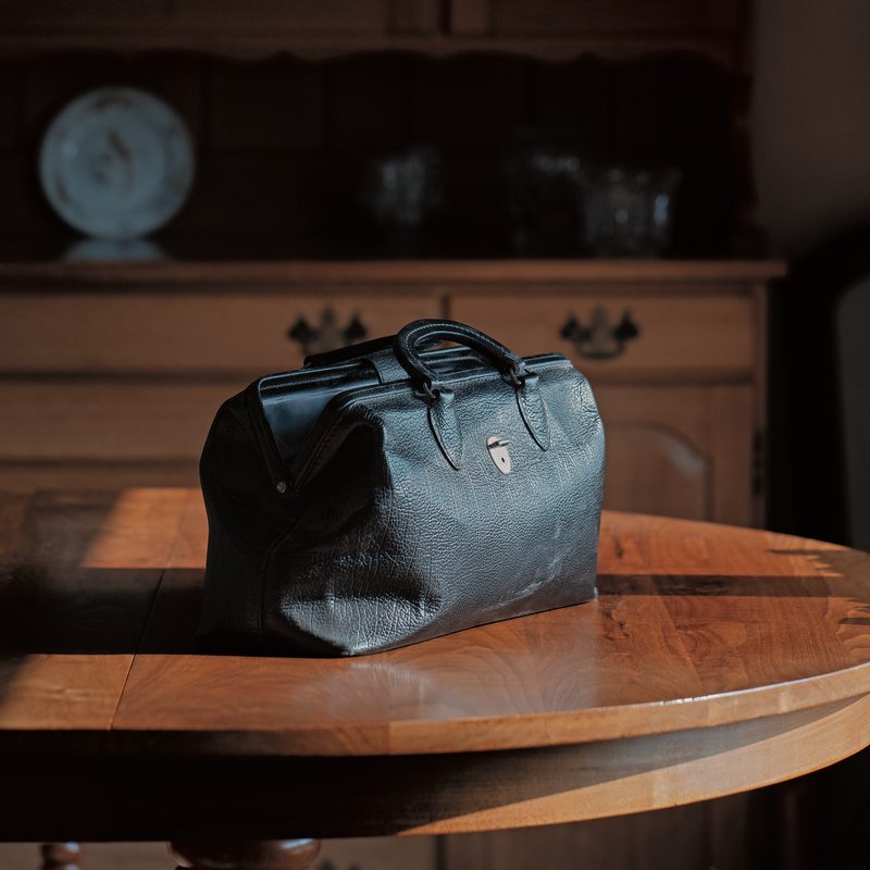 A vintage doctor's bag sits on a wooden table in a farm house