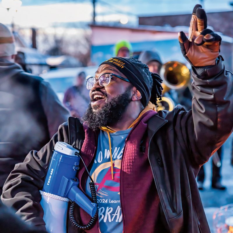A man with a megaphone leads a brass band on a winter street