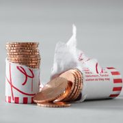 A cracked open roll of pennies which are edge-engraved with the phrase, “THE BODY WAS ALREADY SO FRAGILE”. The image is carefully composed: half of the roll is stacked upright and half is spilling out across a neutral-grey background, which is studio lit.