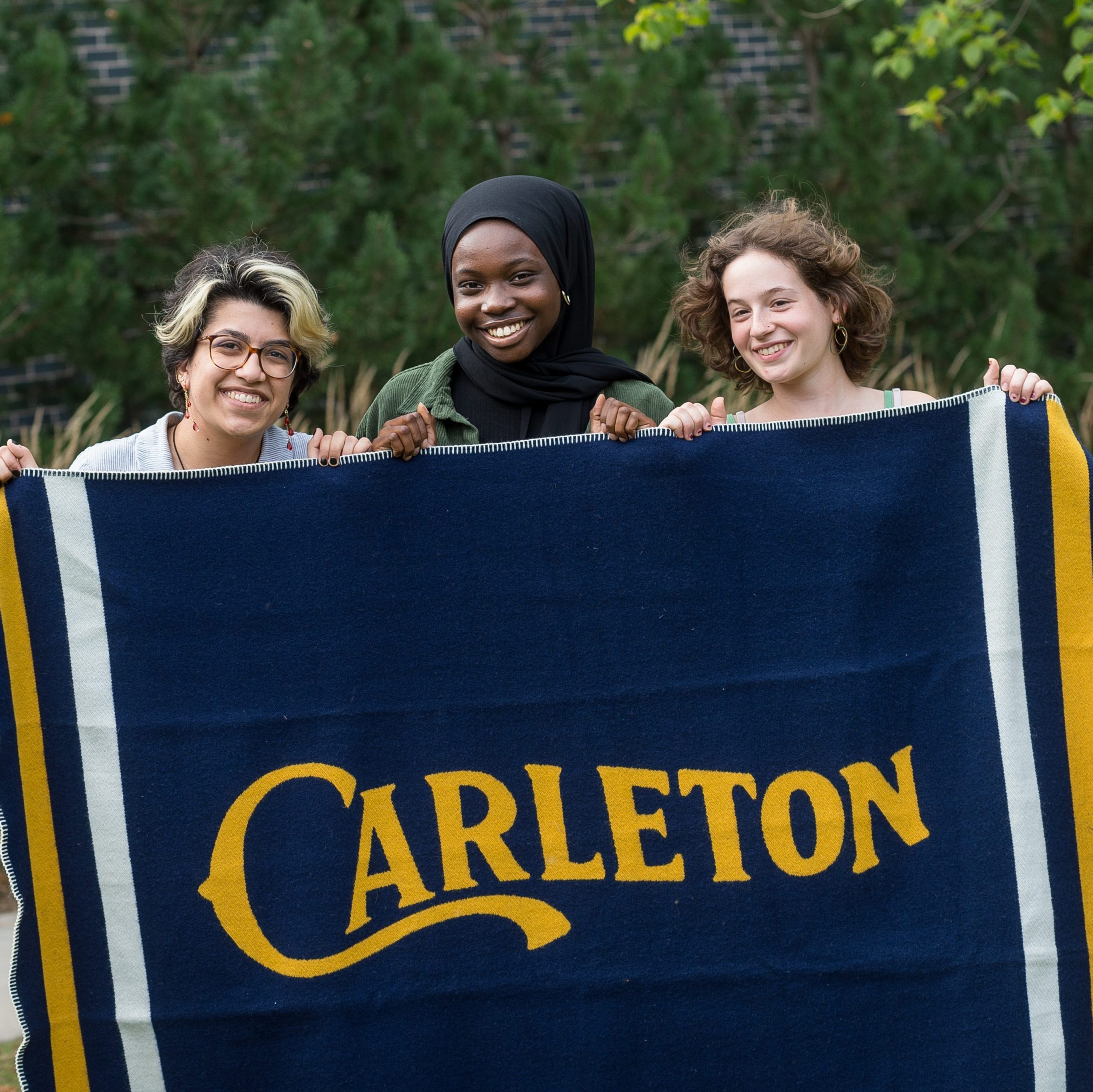 students hold up a large wool Carleton blanket