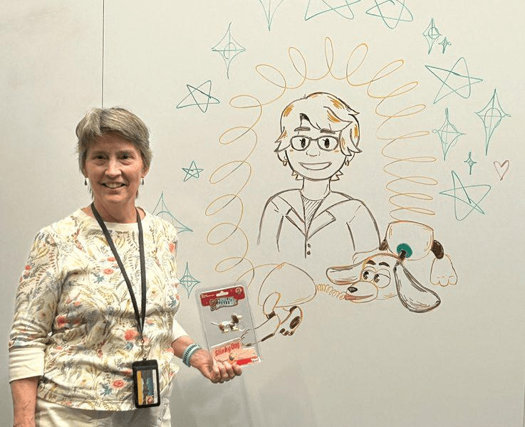 Trish Ferrett holds a Slinky Dog toy while standing in front of a whiteboard with a drawing on it