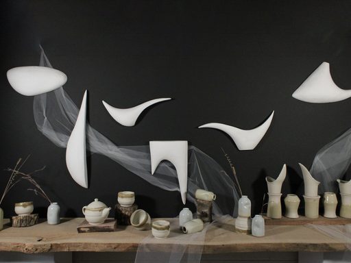 stoneware in various forms arranged on a table, against backdrop of tulle, hanging organic forms