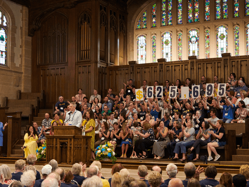 large crowd gathered in Skinner Chapel holding dollar amount sign
