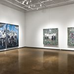 A corner view of three large-scale, woven tapestries mounted to gallery walls. The left textile is a black-and-white image of an officer pointing a gun at a group of men with baseball bats; the background is a wooded area tinted blue. The works on the right wall are a pair which both include black-and-white, historical imagery of figures set against intricate floral backgrounds.The work on the right depicts a funeral procession, and text like a newspaper headline above reads “VOTERS IN REVOLT”.