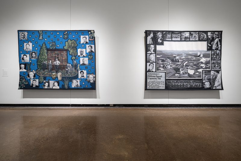 Two large, woven tapestries hang side by side on a wall. The left tapestry has a bright blue background with black and white square headshots scattered throughout. In the middle are four people in front of a bookshelf and trees. The right tapestry is black-and-white and includes a border of square headshots and a newspaper article “Attention- Defence Squad Captains, 544”. The middle depicts an image of a train and landscape photographed from above.