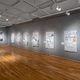 An establishing view of a gallery with wooden floors and grey walls. On the wall hang eight dye-sublimated prints on satin. Their imagery is drawn from historical newspapers, combined with the artist’s illustrations. These artworks track the rise of fascist organizations and ideologies in Minnesota in the 1930s, in particular, the pro-Nazi organization the Silver Legion of America (or Silvershirts).