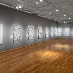 Eight lighted dye-sublimated prints on satin hang in a gallery with gray walls and wooden floors. Imagery includes black-and-white text, images, and graphics.