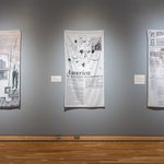 Alt: Three dye-sublimated prints on satin hang side by side in a gray walled art gallery. Imagery includes black-and-white newspaper headline and text, line drawn graphics, and black and white photographs.