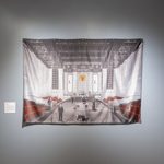 A dye-sublimated print on satin includes a number of prominent businessmen and government officials politically active in Minnesota in the 1930s. Small white text above each figure identifies who they are. of the time in a large stone room with elaborate decorative ceiling and rows of red seating on the left and right. Imagery throughout includes bloody deer carcasses, rifles, and American flags.