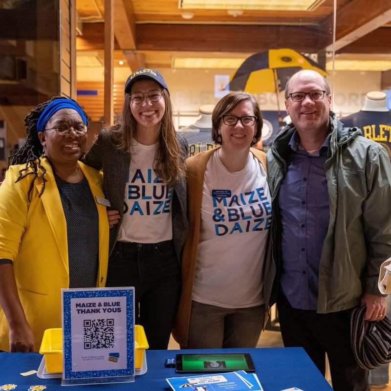 Three women and a man smile for the camera while wearing Carleton College apparel.