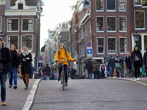 A woman rides a bike through a hilly street in Amsterdam