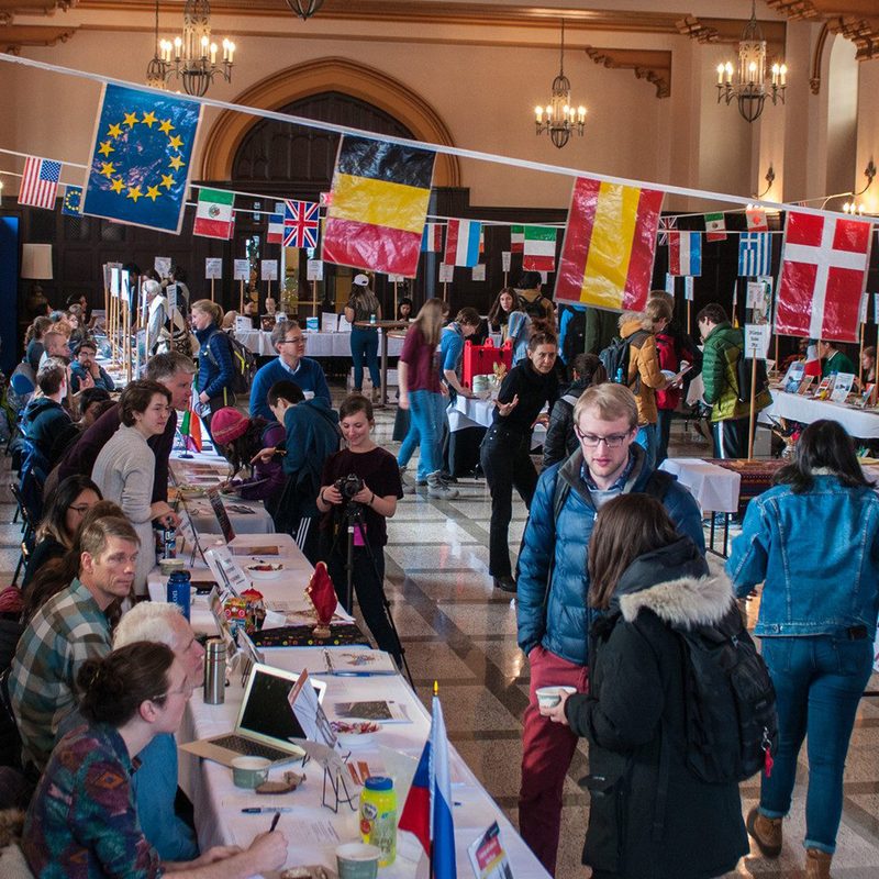 Students and professors at the Off Campus Studies World's Fair, with banners showing the flags of many nations