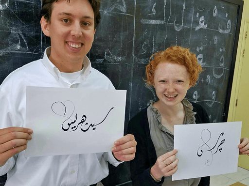 Seth Harris '18 and Gray Babbs '18 hold sheets of paper with Arabic calligraphy in front of a chalkboard