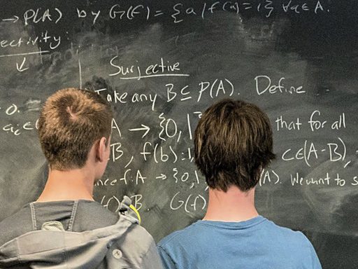 two students look at a mathematical proof on a chalkboard