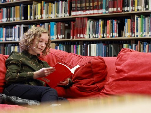 A student reads a book on a couch in Gould Library
