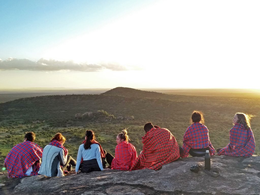 A group of students on an anthropology study abroad program in Tanzania sit on a mountain to watch the sun rise