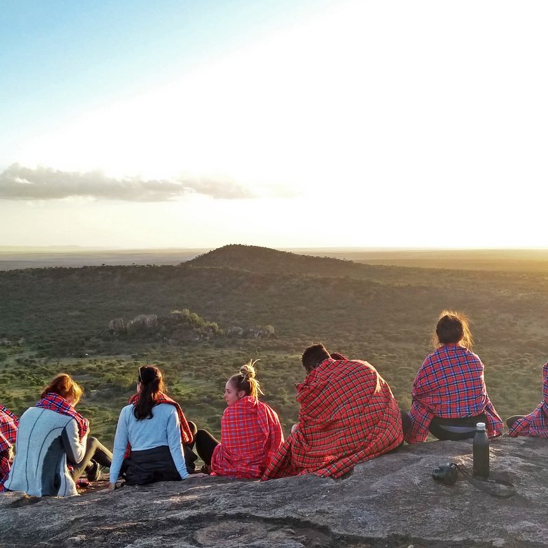 A group of students on an anthropology study abroad program in Tanzania sit on a mountain to watch the sun rise