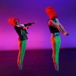 Two dancers wearing wigs and jumping