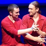 Two dancers wearing red and smiling at each other