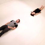 A man and a woman laying on a white floor with their feet on opposite walls