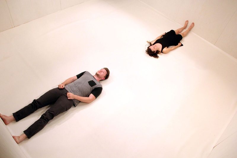 A man and a woman laying on a white floor with their feet on opposite walls