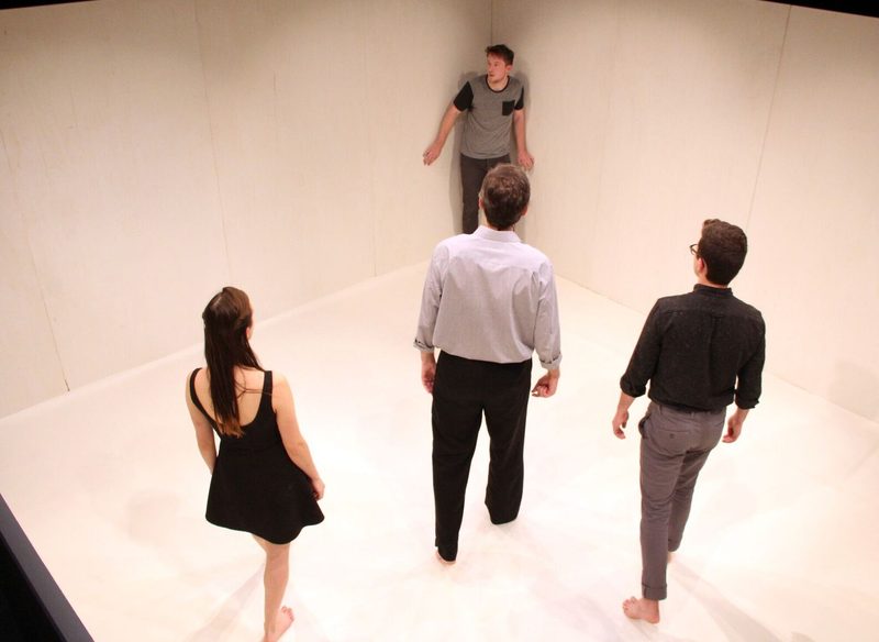 Man being cornered in an empty white room by three other actors