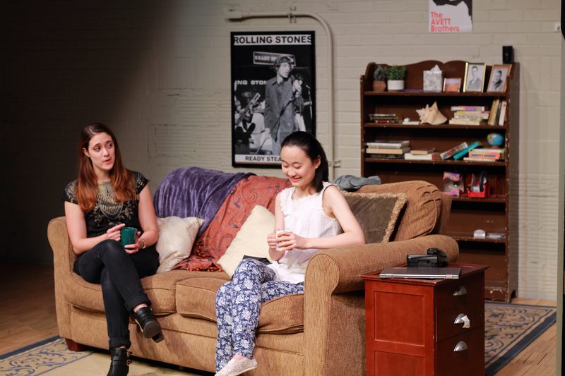 Two women sitting on a couch, holding coffee cups and smiling