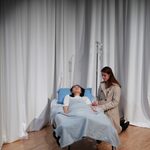 A woman kneeling next to a woman asleep in a hospital bed