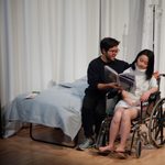 A man reading to a woman in a wheelchair in a hospital room