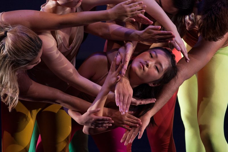 Dancers reaching towards another dancer's face