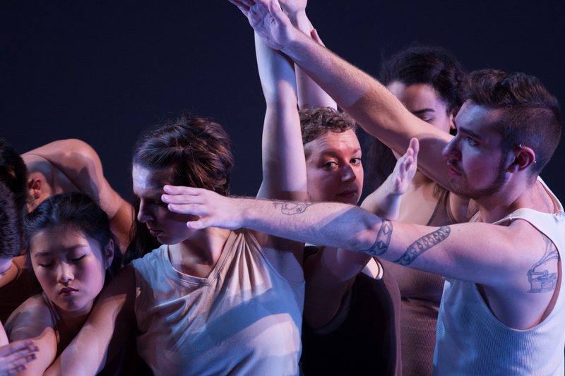 Dancers huddled together, some with their arms up