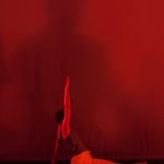 A dancer doing the splits with her arm raised under a red light
