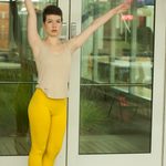 A dancer wearing yellow pants and standing with her arms up