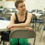 A dancer kneeling on a chair and looking off camera