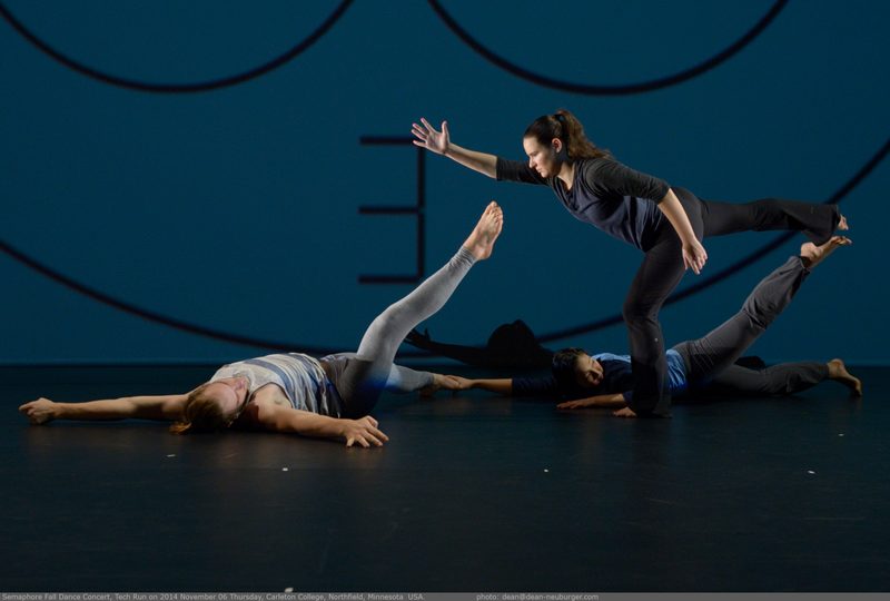 A dancer standing on one leg next to dancers lying on the floor