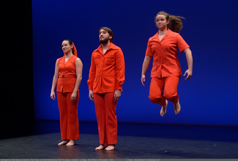 Dancers on stage wearing orange, one dancer jumping