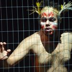 A shirtless man in a cage, wearing face paint