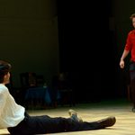 A man in a red shirt running over to a man in a white shirt sitting on the floor