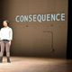 Girl standing on stage and the word "consequence" projected behind her